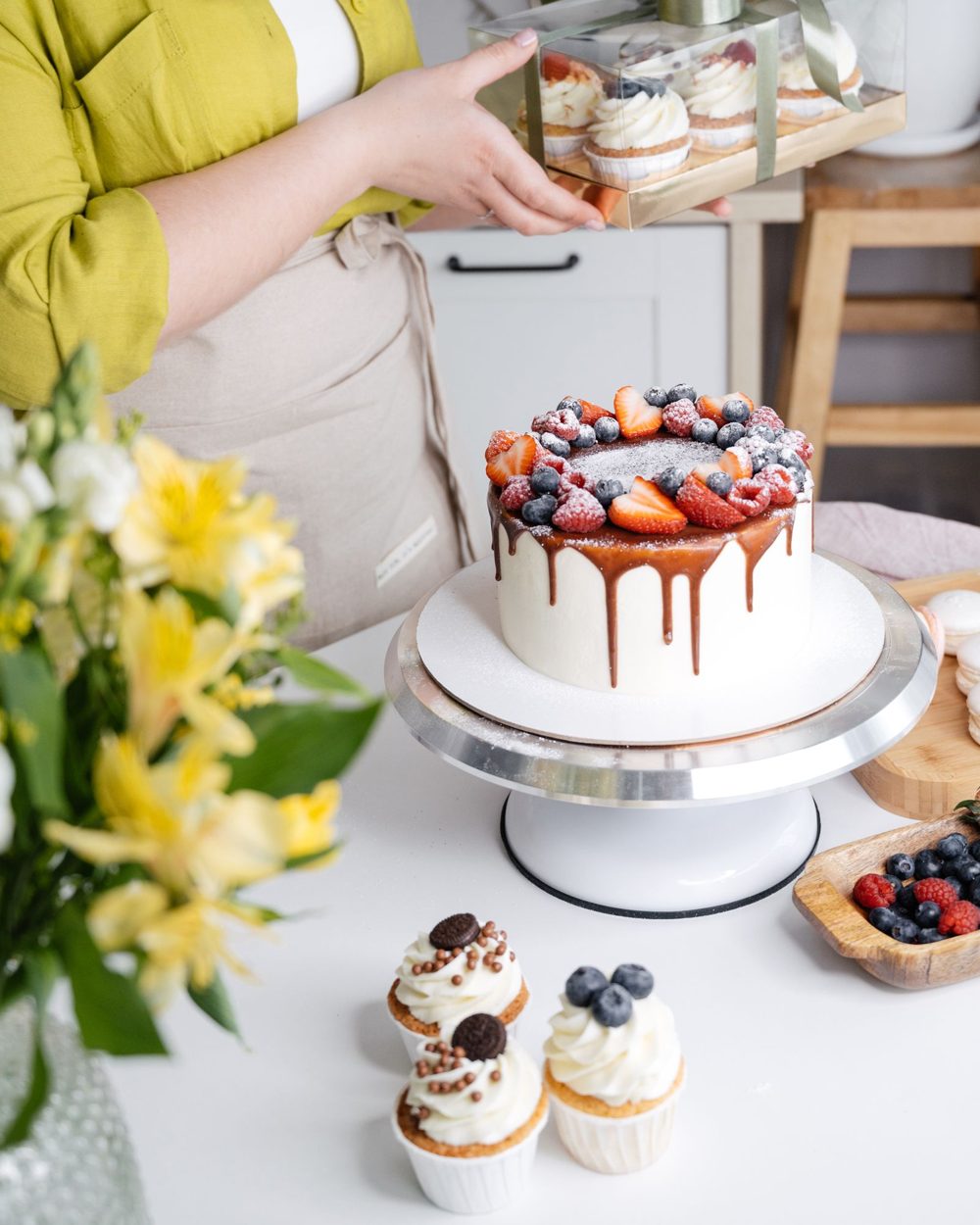 A baker with a caramel drip cake topped with berries and two cupcakes: a sweet, fruity pairing when you choose a cake flavour