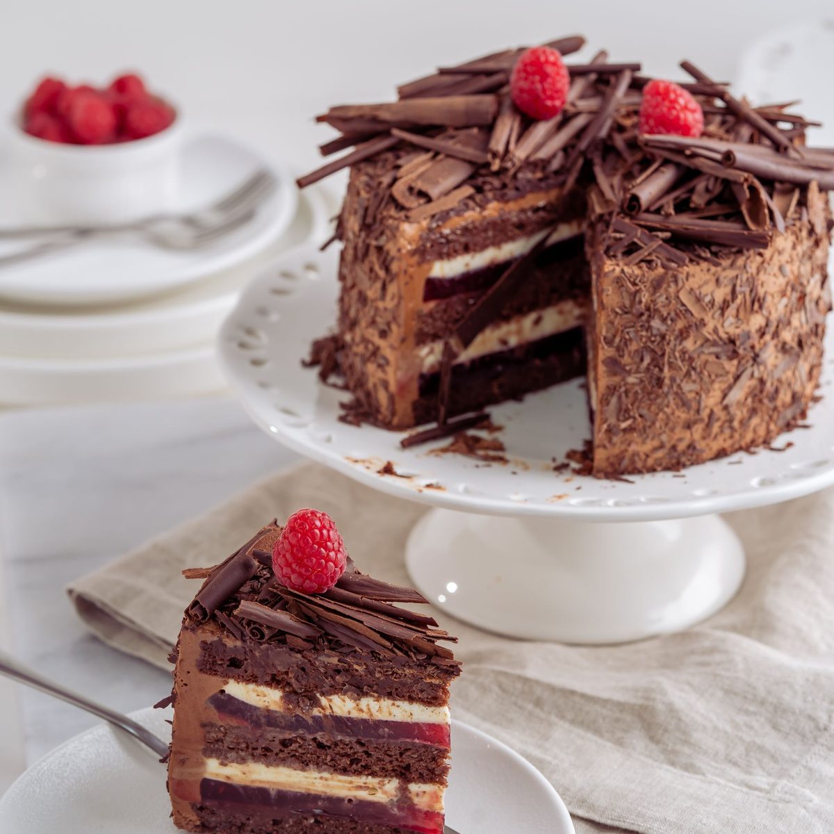 A chocolate layer cake on a white cake stand with one slice cut and plated