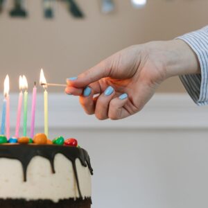 A hand lighting the candles on a chocolate drip birthday cake