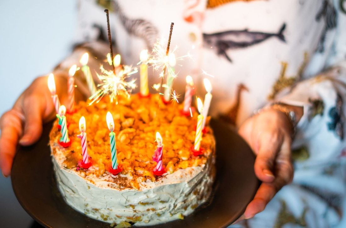 Hands holding a birthday cake with candles and a sparkler: plan the details early when you order a birthday cake